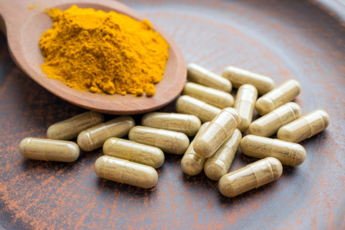 Natural herb food supplement turmeric veggie capsules and spoon with orange curcumin powder on clay plate. Organic Turmeric extract, Curry Extract, Diferuloylmethane, JiangHuang, Curcuma Longa CURCUMA