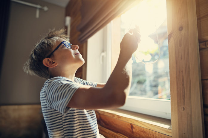 Little boy opening the roller blinds in the morning finestre