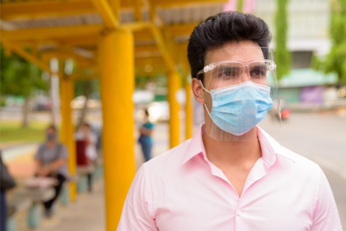 young-indian-businessman-with-mask-and-face-shield-waiting-at-the-bus-picture-id1249994728 occhi visiera covid