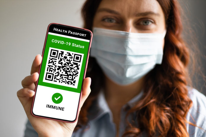 Covid-19 Health Passport. Traveler woman wearing a face mask holding a passport, ticket pass and smartphone with digital health passport app. GREEN PASS CONDOMINIO