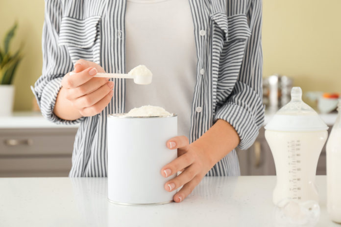 Woman preparing baby milk formula at table in kitchen latte artificiale