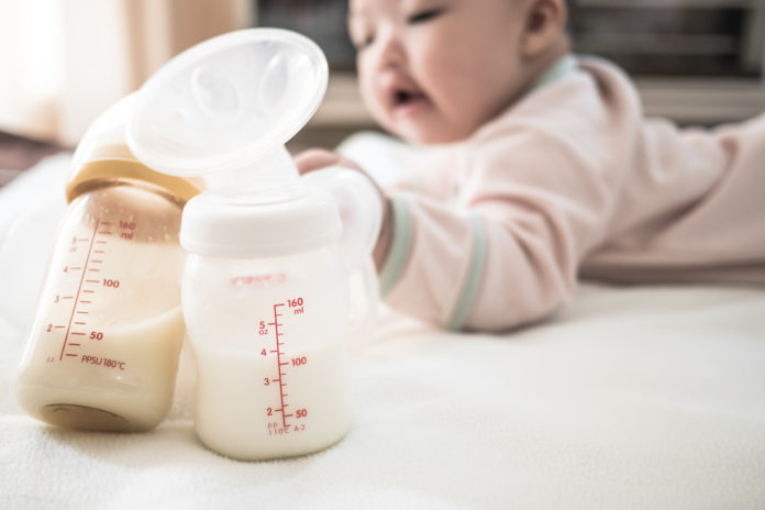 Close-up Of Milk Bottles Against Baby Girl On Bed At Home LATTE MATERNO