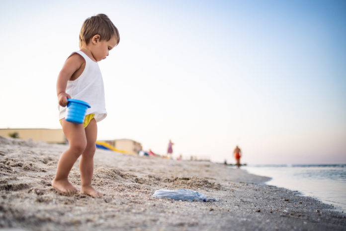 Boy playing with toys on the beach building beads and turrets smiling at someone behind the scenes on summer vacation BAMBINI AL MARE