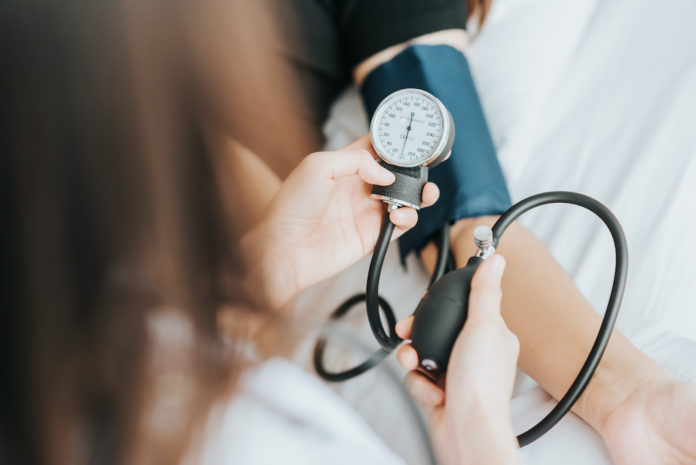 Back view of doctor checking blood pressure of a patient with sphygmomanometer in bed ipertensione