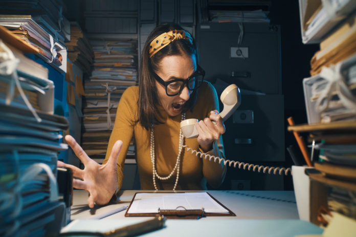 Stressed secretary shouting at the telephone receiver