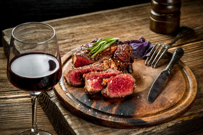 Grilled ribeye beef steak with red wine, herbs and spices on wooden table MITI