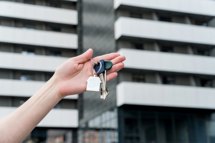 Keys with a keychain in a female hand in front of apartment house. AFFITTO