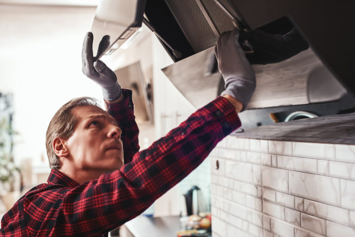 First technical aid. Close-up of young man repairs exhaust hood PULIRE LA CAPPA