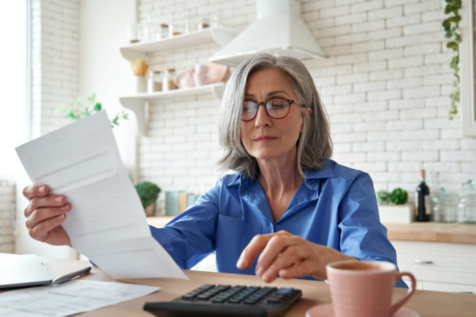 Mature woman holding paper bill using calculator managing finances at home. QUOTA 103