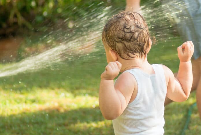 Child playing under sprinkler / hose on a hot day CALORE BAMBINI