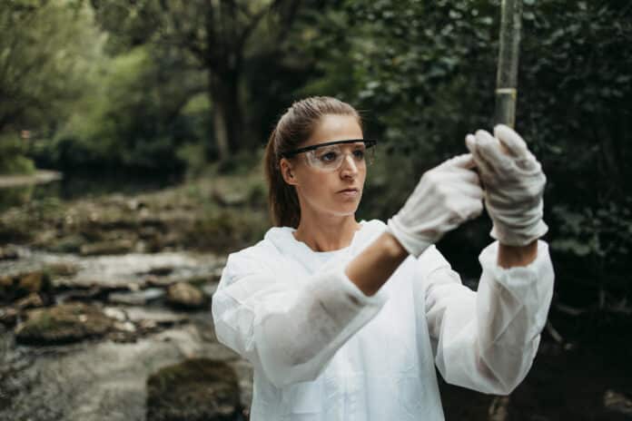 pfas Female scientist biologist and researcher in protective suit taking water samples from polluted river. pesticidi pfas