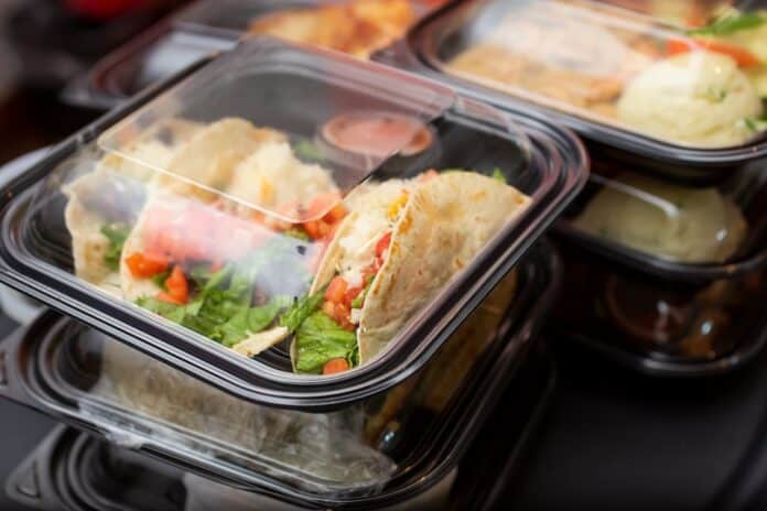 A view of several entrees prepared inside to-go plastic containers, ready for take out orders, in a restaurant setting. plastica