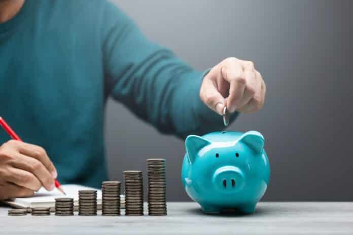 Man is dropping coins into a blue piggy bank, symbolizing the act of saving and financial responsibility. Financial planning, budgeting, and building a stable future through consistent savings contributi