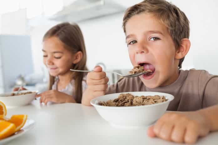 Boy eating cereal while having breakfast with his sister in the kitchen