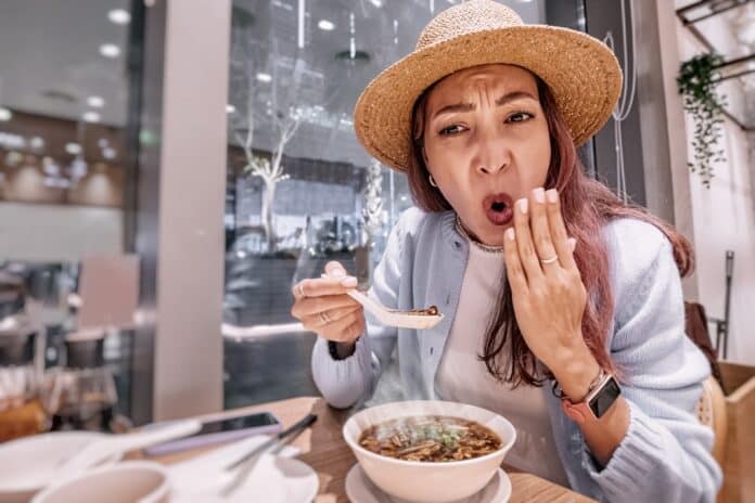 Tourist enjoying traditional food in a chinese restaurant, surprised by the taste of hot and spicy soup caldo
