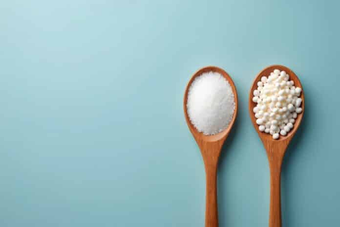 DOLCIFICANTI PUBERTà PRECOCEWooden spoons with sugar, sweetener on blue background. White sugar versus artificial sweetener. Concept of choosing right kind of sweetener. Food rich in carbohydrates. Comparison of sweet DOLCIFICANTI PUBERTà PRECOCE