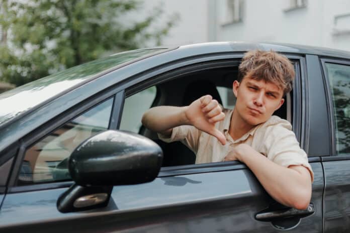 RC-AUTO NEOPATENTATI Sad young driver showing thumbs down in car. Bad customer service by repair shop RC-AUTO NEOPATENTATI