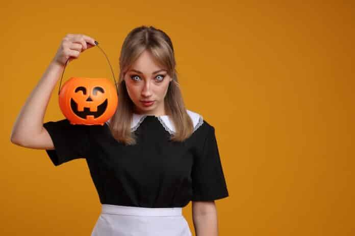 Woman in scary maid costume with pumpkin bucket on orange background, space for text. Halloween celebration HALLOWEEN