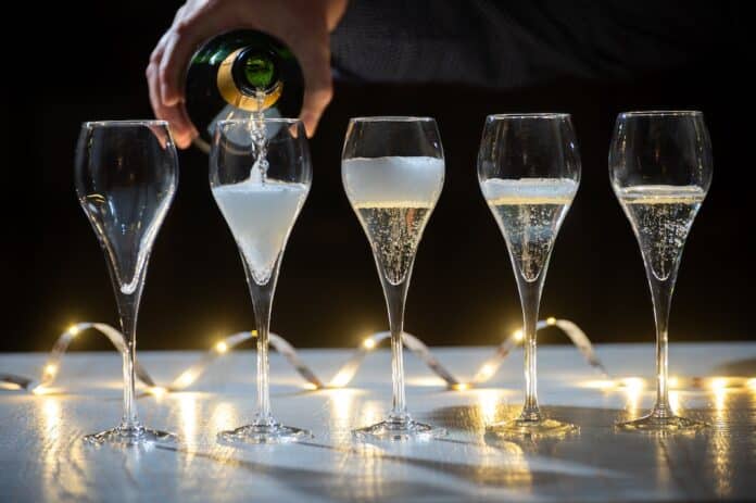 New year party, pouring of brut champagne bubbles cava or prosecco wine in tulip glasses with garland lights on background prosecco