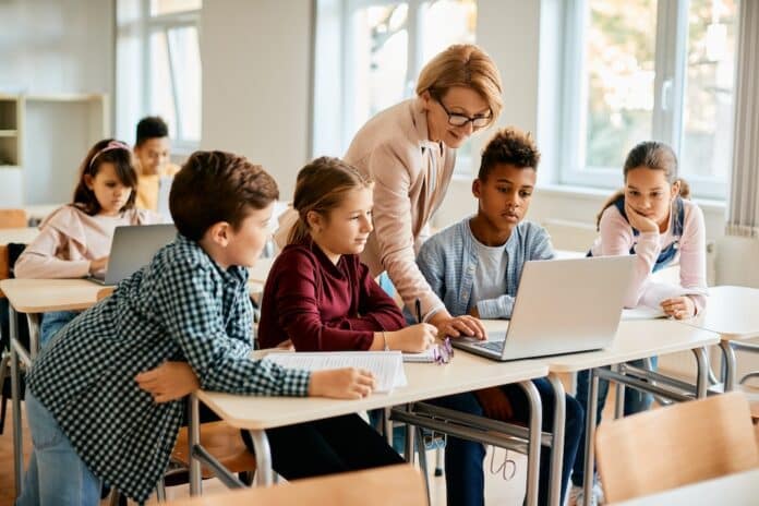 Multiracial group of elementary students having computer class with their teacher in classroom. scuola registro