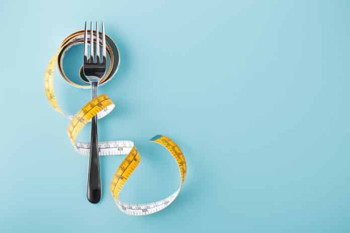 Fork with measuring tape around, diet background DIETA MIMA DIGIUNO