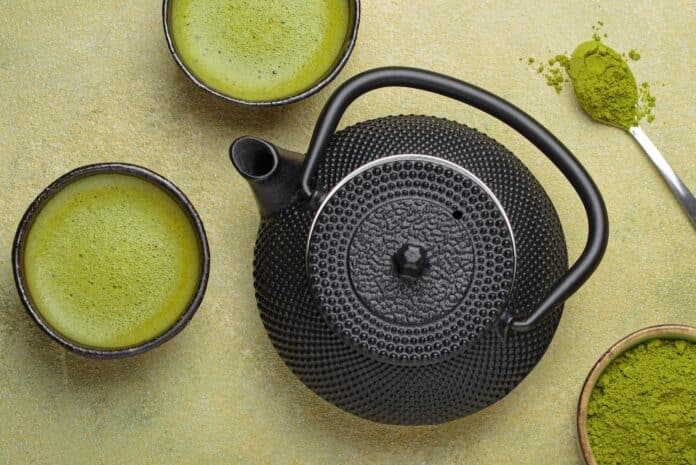Matcha tea powder and hot drink in bowls with black iron teapot on green background, Japanese tea top view MATCHA