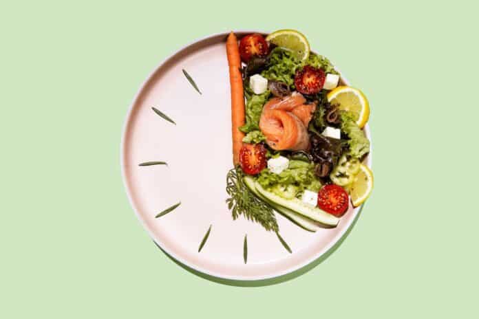 intermittent fasting concept plate as a clock with salad, salmon, fish and vegetables, tomato, lemon dieta diete