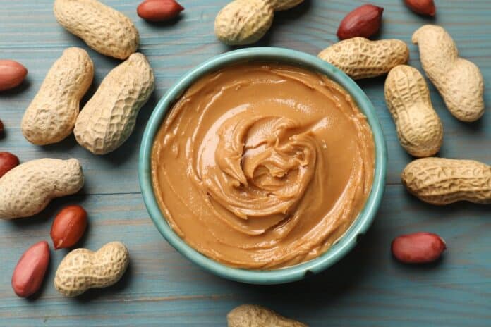 Tasty peanut butter in bowl and groundnuts on light blue wooden table, flat lay arachidi