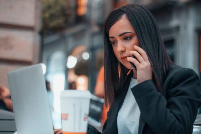 Asesora realizando una llamada telefónica con su telefono móvil a un cliente para comentar diversos asuntos sobre su trabajo en una cafeteria por la mañana tomando café y mirando el portátil tim