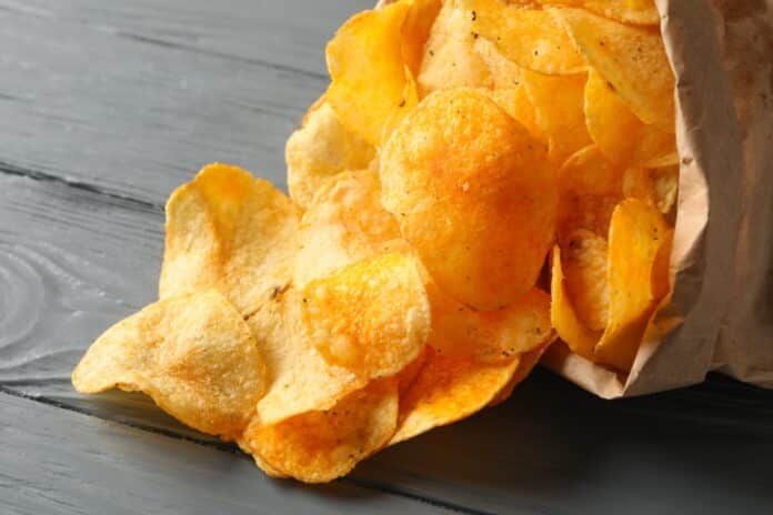 Paper bag of potato chips on gray wooden background, space for text. Closeup chips