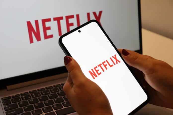 NETFLIX Salvador, Brazil - April 14, 2026: Woman holding smartphone with Netflix logo on screen. Netflix streaming on laptop and smartphone. NETFLIX