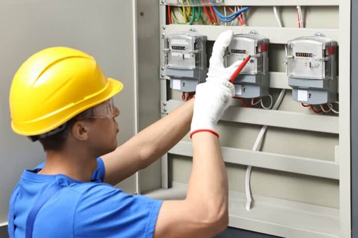 Electrician with screwdriver checking electrical meter indoors
