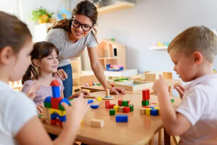 Preschool teacher with children playing with colorful wooden didactic toys at kindergarten CENTRI ESTIVI