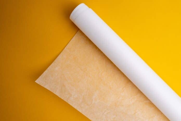 Plastic wrap, aluminum foil and a roll of parchment paper on a yellow background. Gadgets for the kitchen and packaging.