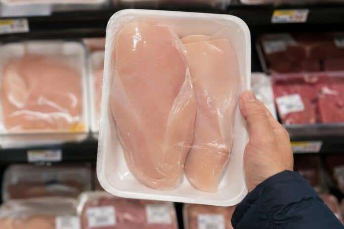 Person holding packaged raw chicken breast in supermarket aisle among meat products on display. concept of grocery shopping, food selection, fresh poultry, consumer choice, meal preparation pollo, polli