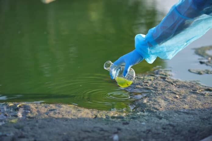 Close-up environmentalist hand of a researcher in a process of taking a sample of contaminated water from a lake goletta