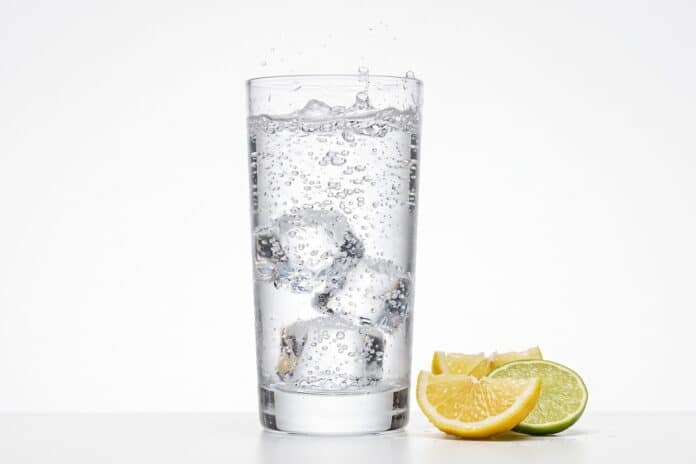 Refreshing sparkling water with ice cubes in a tall glass, clear soda with lemon and lime wedges, cold carbonated beverage for summer hydration isolated on White Background cola