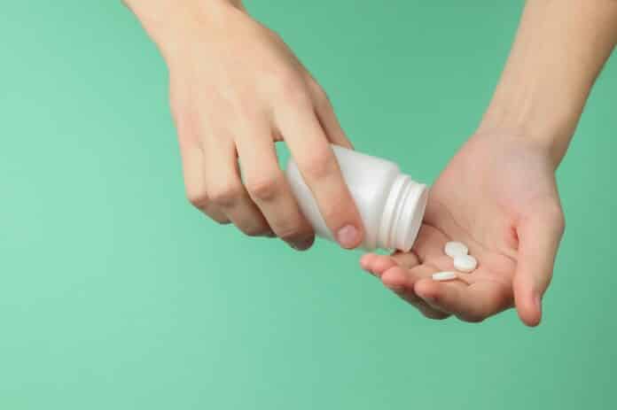 Female hands is holding white pill bottle and pills on blue background. Health. Disease. pillole