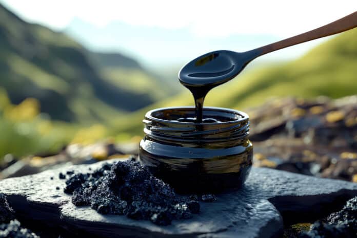 An open black jar of liquid Shilajit resin on a rocky surface. A jar with a spoon scooping and pouring black liquid Shilajit resin back into the jar. Black solid shilajit stones are placed nearby. Shilajit