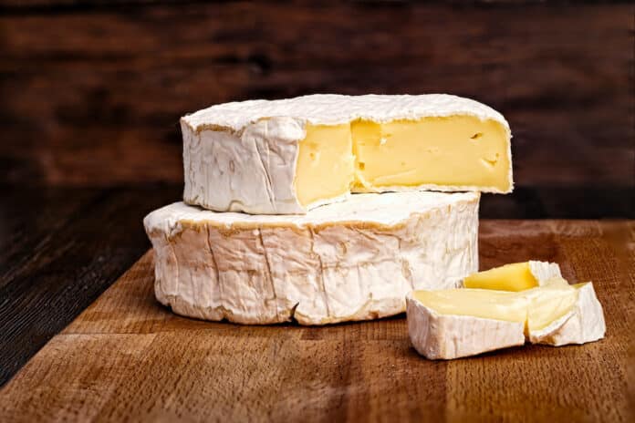 Whole and sliced Camembert cheese on rustic wooden board with dark background